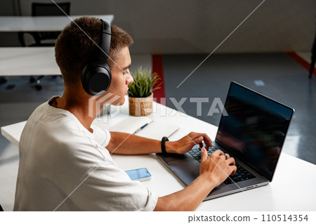 Young man wearing headphones while studying with laptop 110514354