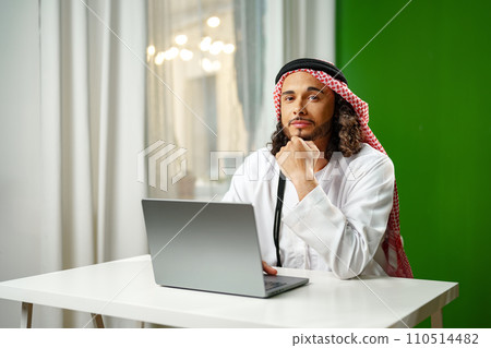 Young Arab man in traditional dress thobe working on computer in office Young Arab man in traditional dress thobe working on computer in office 110514482