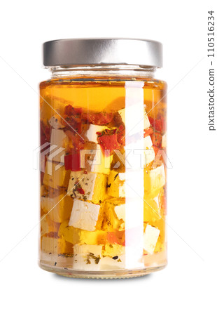 Feta cubes in oil, with red pepper and chili pieces, in glass jar. Greek cheese, matured in brine, with soft, moist texture, fresh, salty and acidic taste, cut in block shape, preserved in spiced oil. 110516234