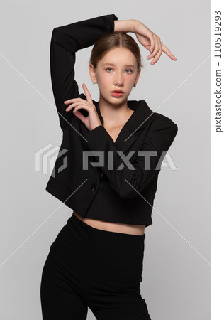 In a black fashionable suit, a young girl poses against a gray background. 110519293