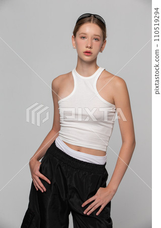 A young beautiful girl fashion model in a white top is posing on a gray background. A young beautiful girl fashion model in a white top is posing on a gray background. 110519294