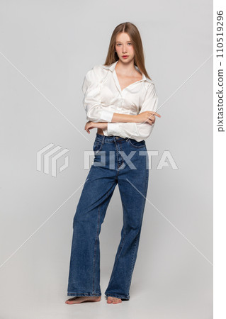 Young girl in jeans and a white shirt on a gray background. 110519296