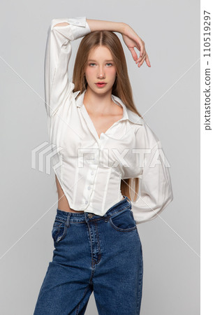 Portrait of a beautiful blonde girl with long hair. She poses for the camera in a white shirt and jeans. Portrait of a beautiful blonde girl with long hair. She poses for the camera in a white shirt and jeans. 110519297