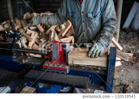 Man with work gloves cuts firewood with hydraulic log splitter Man with work gloves cuts firewood with hydraulic log splitter 110519541