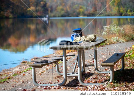 Picnic table with fishing gear and two rods boaters in background lake Picnic table with fishing gear and two rods boaters in background lake 110519549