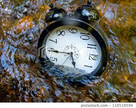 A large alarm clock half submerged in a beautiful flowing stream 110519594