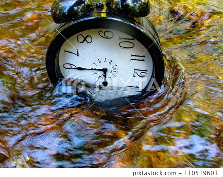 A large alarm clock half submerged in a beautiful flowing stream A large alarm clock half submerged in a beautiful flowing stream 110519601