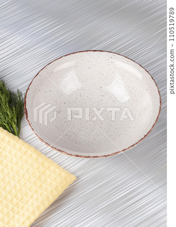 White empty deep clay plate with a spoon on a gray background. 110519789