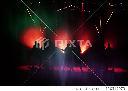 Dark silhouettes of dancing people against the background of the lazar light lights of the stage. 110519973
