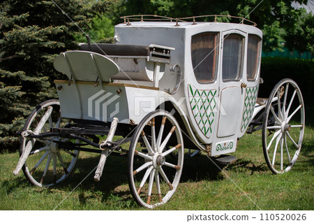 An antique white carriage from the nineteenth century on a green lawn. The prototype of a modern car. An antique white carriage from the nineteenth century on a green lawn. The prototype of a modern car. 110520026