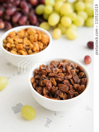 Bowls of green and red dark raisins with ripe raw grapes on light background. Bowls of green and red dark raisins with ripe raw grapes on light background. 110521019