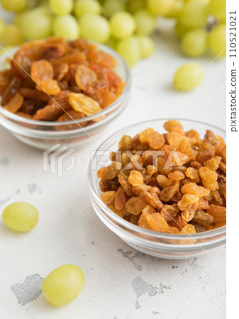 Dried sweet green raisins in glass bowl with ripe grapes on light kitchen background. 110521021