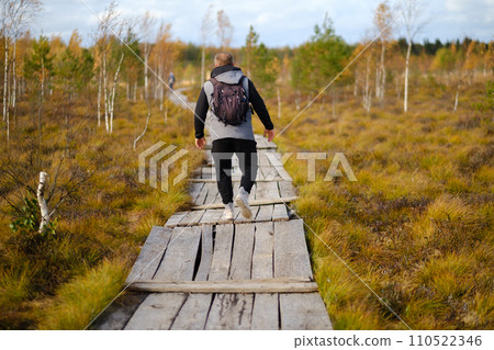 A man with a backpack walks along a wooden path in a swamp in Yelnya, Belarus A man with a backpack walks along a wooden path in a swamp in Yelnya, Belarus 110522346