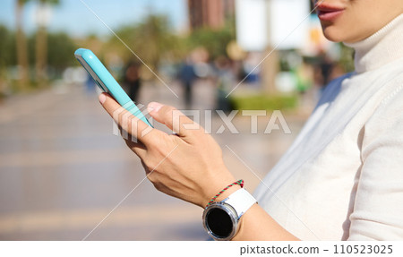 Woman's hand with smart wrist watch, checking new mobile app on smart phone, browsing web site, online communication Woman's hand with smart wrist watch, checking new mobile app on smart phone, browsing web site, online communication 110523025