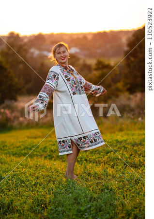 Embroidered and unique petticoat, a girl walks barefoot in the field in an embroidered shirt. Embroidered and unique petticoat, a girl walks barefoot in the field in an embroidered shirt. 110523922