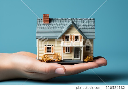 A man's hand holds a small house, a miniature of a family home. 110524182