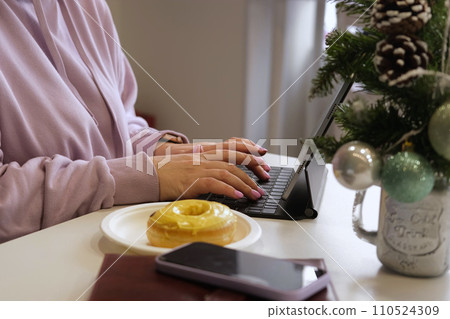 Working online during Christmas. Young cheerful blonde female in warm hoody smiling while chatting with friends using her laptop, sitting in cozy cafe. Winter holidays. Businesswoman, graphic designer 110524309