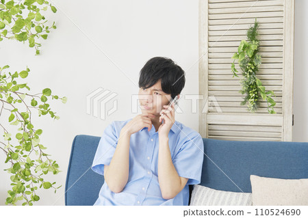 A man calling on his smartphone while worrying at home A man calling on his smartphone while worrying at home 110524690