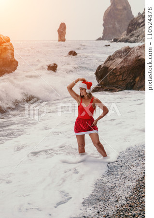 Woman summer travel sea. Happy tourist in red bikini and Santas hat enjoy taking picture outdoors for memories. Woman traveler posing on the beach surrounded by volcanic mountains, sharing travel joy Woman summer travel sea. Happy tourist in red bikini and Santas hat enjoy taking picture outdoors for memories. Woman traveler posing on the beach surrounded by volcanic mountains, sharing travel joy 110524878