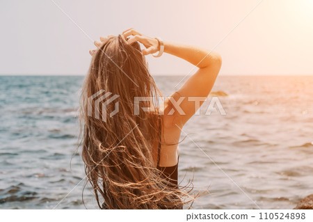 Woman summer travel sea. Happy tourist in hat enjoy taking picture outdoors for memories. Woman traveler posing on the beach at sea surrounded by volcanic mountains, sharing travel adventure journey 110524898