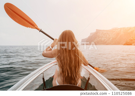 Woman in kayak back view. Happy young woman with long hair floating in transparent kayak on the crystal clear sea. Summer holiday vacation and cheerful female people relaxing having fun on the boat Woman in kayak back view. Happy young woman with long hair floating in transparent kayak on the crystal clear sea. Summer holiday vacation and cheerful female people relaxing having fun on the boat 110525086