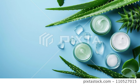 Natural aloe skincare flat lay, glass containers with gel and creams, surrounded by aloe vera leaves. Blue background 110527015