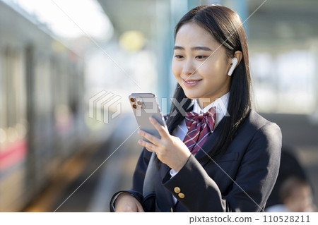 High school girl wearing earphones looking at smartphone screen, focus on hands 110528211