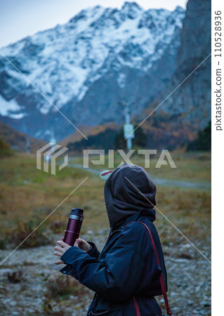 Girl drinking coffee from a thermos on the background of a glacier in the mountains Girl drinking coffee from a thermos on the background of a glacier in the mountains 110528936