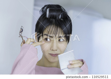 A young woman wearing a curler and applying a curler to her eyelashes A young woman wearing a curler and applying a curler to her eyelashes 110529511
