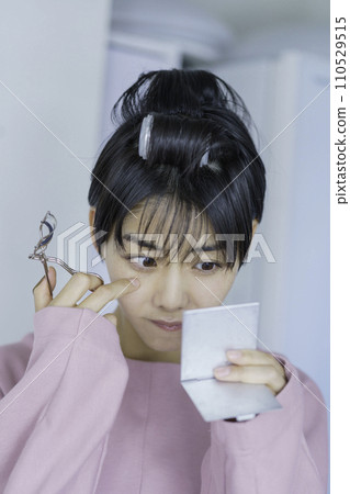 戴著捲髮器並將捲髮器應用於睫毛的年輕女性，垂直位置 110529515
