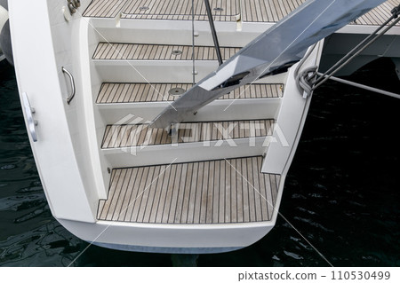 Stern of super luxury yacht berthed in marina. Teak deck on stern of sailing boat. Teak stairs ladder on motor boat. Aft part. Yachting concept. 110530499
