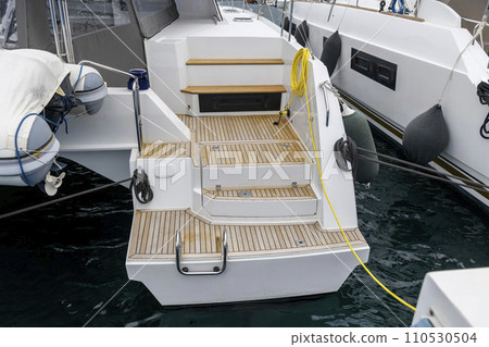 Stern of super luxury yacht berthed in marina. Teak deck on stern of sailing boat. Teak stairs ladder on motor boat. Aft part. Yachting concept. 110530504