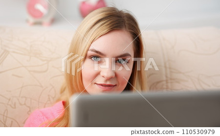 young beautiful blond woman sit on the sofa in livingroom hold tablet in arms young beautiful blond woman sit on the sofa in livingroom hold tablet in arms 110530979