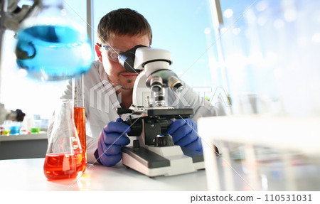 Portrait of a young chemist looking in binocular 110531031