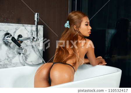 Young topless woman sitting in white bath with blue water Young topless woman sitting in white bath with blue water 110532417
