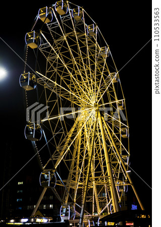 Part of ferris wheel against a blue sky background with lights neby night lighting 110533563
