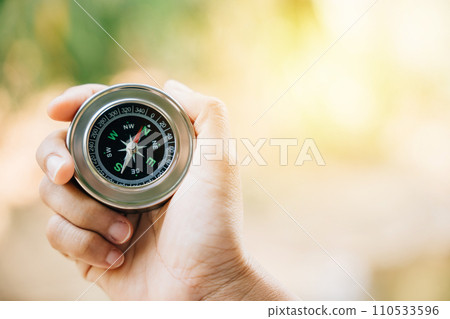 In the forest a hiker navigates confusion with a compass in hand. The compass grasped by the traveler represents topography and discovery in the midst of nature beauty. 110533596
