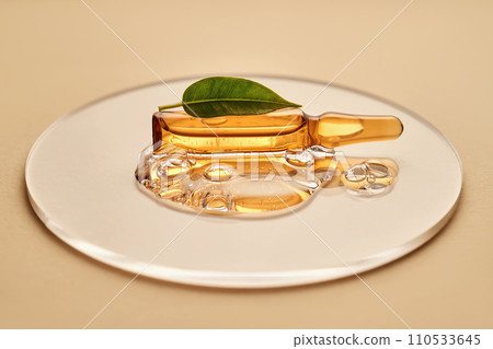 Ampoule in a drop of cosmetic gel on a beige background. 110533645