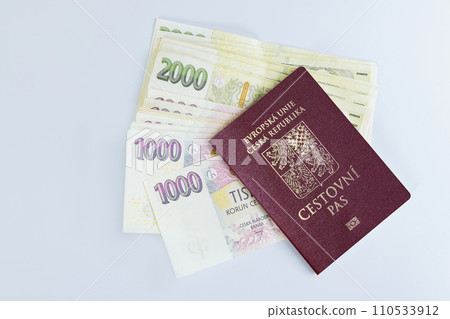 Various denominations of CZK koruna banknotes are stacked on white background with Czech passports in foreground 110533912