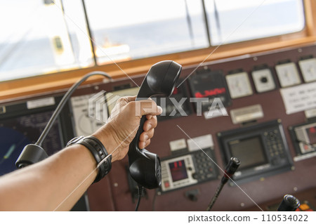 Navigational control panel and VHF radio with hand. Radio communication at sea. Working on the ship's bridge. Navigational control panel and VHF radio with hand. Radio communication at sea. Working on the ship's bridge. 110534022