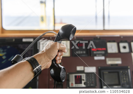 Navigational control panel and VHF radio with hand. Radio communication at sea. Working on the ship's bridge. 110534028