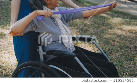 Young nurse or physiotherapist in scrubs helping a happy retired old woman do fitness exercises with light weight dumbbells at home. Concept of physiotherapy for seniors Young nurse or physiotherapist in scrubs helping a happy retired old woman do fitness exercises with light weight dumbbells at home. Concept of physiotherapy for seniors 110534595