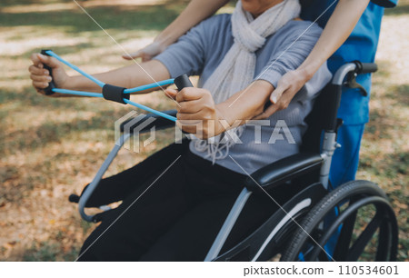 Young nurse or physiotherapist in scrubs helping a happy retired old woman do fitness exercises with light weight dumbbells at home. Concept of physiotherapy for seniors Young nurse or physiotherapist in scrubs helping a happy retired old woman do fitness exercises with light weight dumbbells at home. Concept of physiotherapy for seniors 110534601