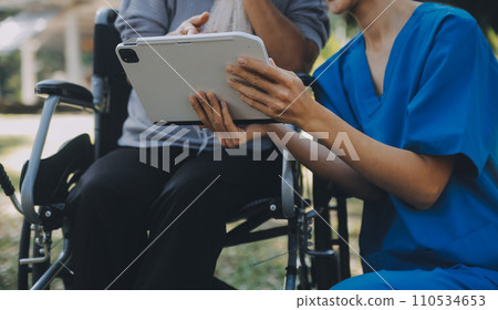 Elderly asian senior woman on wheelchair with Asian careful caregiver and encourage patient, walking in garden. with care from a caregiver and senior health insurance in sun light 110534653