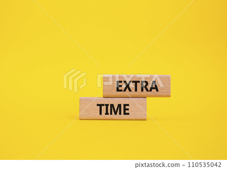 Extra time symbol. Concept word Extra time on wooden blocks. Beautiful yellow background. Business and Extra time concept. Copy space Extra time symbol. Concept word Extra time on wooden blocks. Beautiful yellow background. Business and Extra time concept. Copy space 110535042