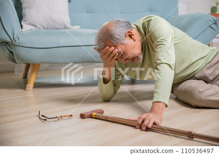 Asian senior man falling down lying on floor at home alone with wooden walking stick in living room, Elderly man headache after fall down, Health care and medicine concept 110536497
