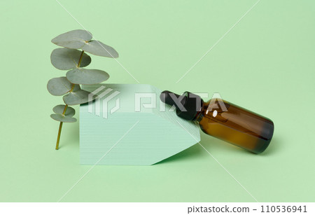 A glass brown bottle with a dropper on a green background, a container for cosmetic products. A glass brown bottle with a dropper on a green background, a container for cosmetic products. 110536941