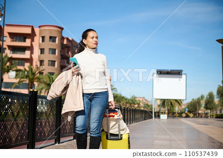 Young woman tourist carrying suitcase, going to hotel or searching the train station using online map on her smart phone 110537439