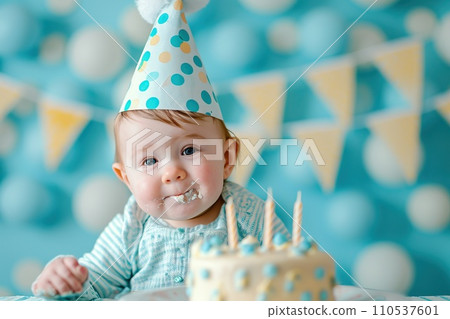 First birthday baby boy party. Boy in a birthday hat, sitting at a table in front of a cak 110537601