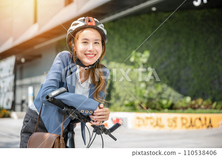 In the city an Asian businesswoman helmeted and in a suit stands with her bicycle ready for a cheerful morning commute to the office. This image combines work and outdoor fun. 110538406
